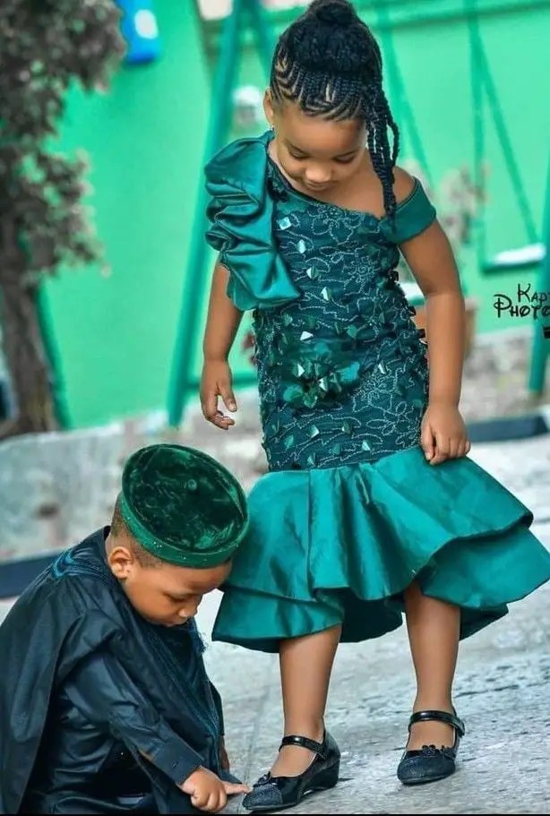 girl wearing a green lace dress looking down at her brother