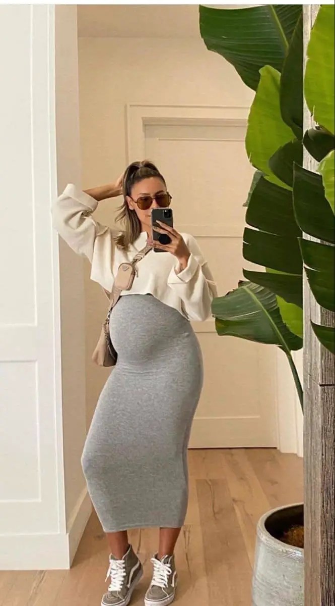 A woman taking a mirror selfie while wearing a top and maternity skirt