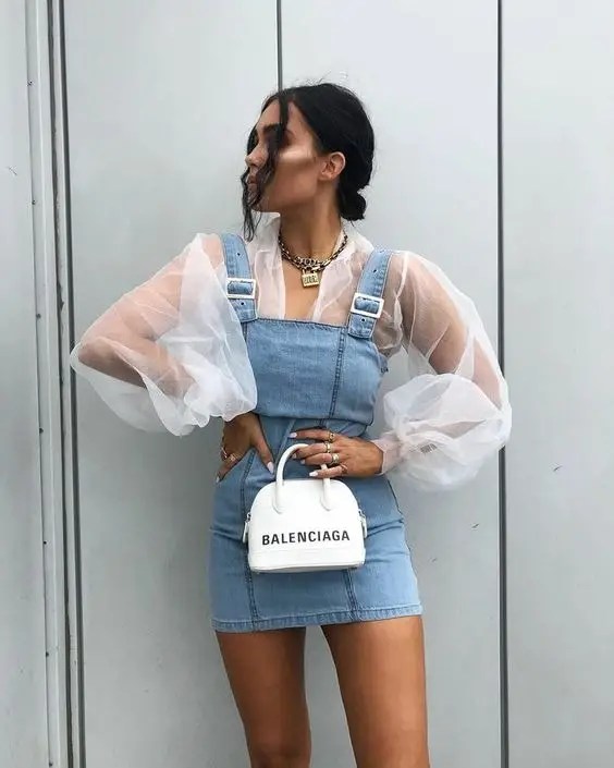 A woman wearing a denim pinafore on a sheer top