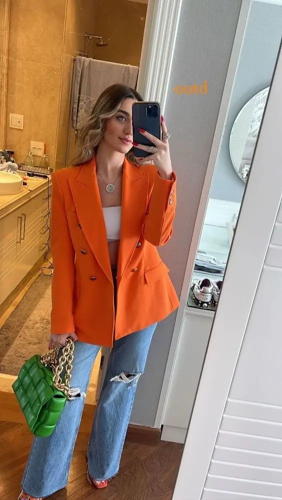 Cute outfit idea for a woman with jeans, an orange blazer and a green handbag