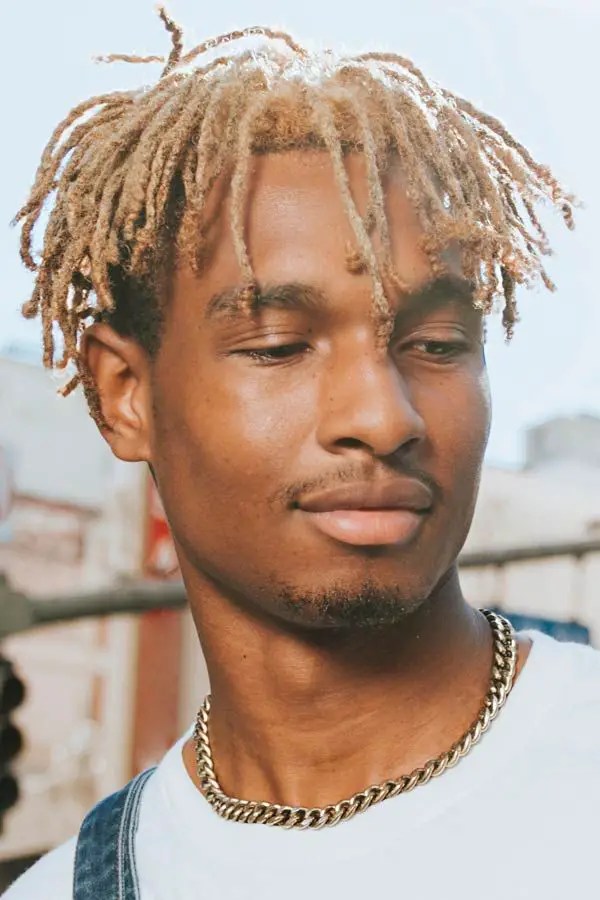 Man rocking blonde dreadlocks with a silver chain around his neck