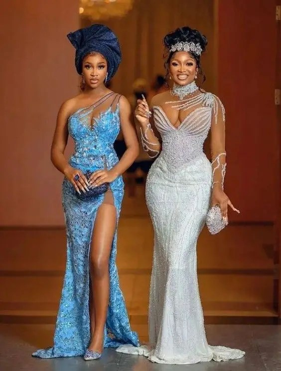 Two women in lace dresses, one blue and one white, each with gel and a tiara