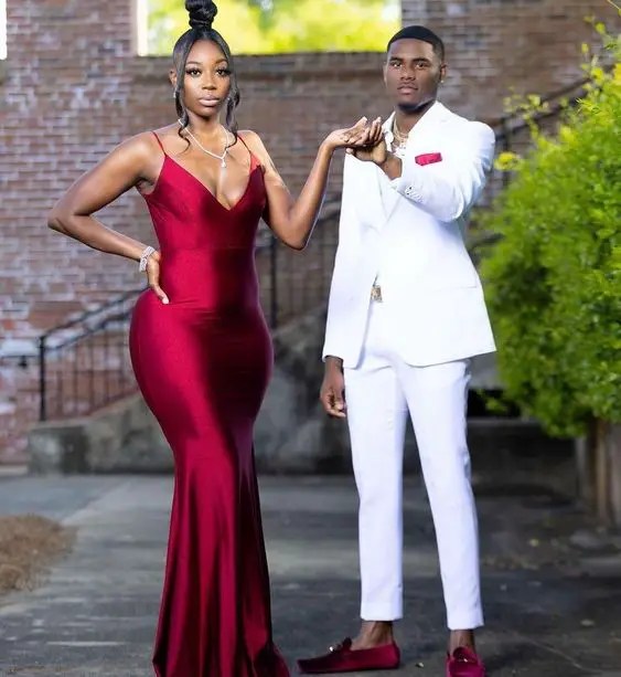 A woman in a burgundy dress and a man in a white suit and red accessories