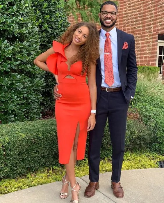 A woman in an orange dress stands next to a man in a navy blue suit