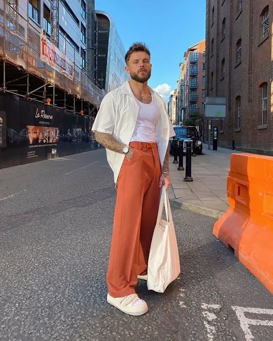 A man wearing a shirt over high-rise pants and carrying a tote bag