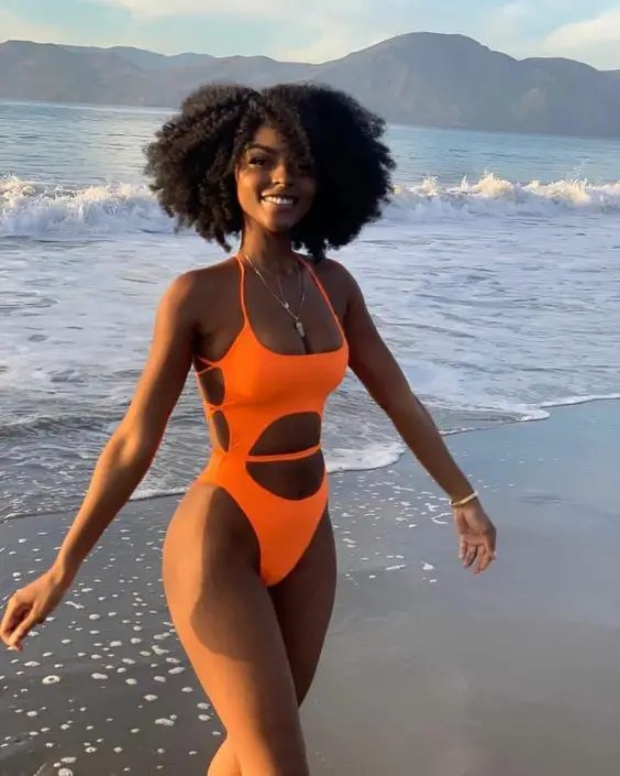 A woman standing on the beach wearing a one-piece swimsuit
