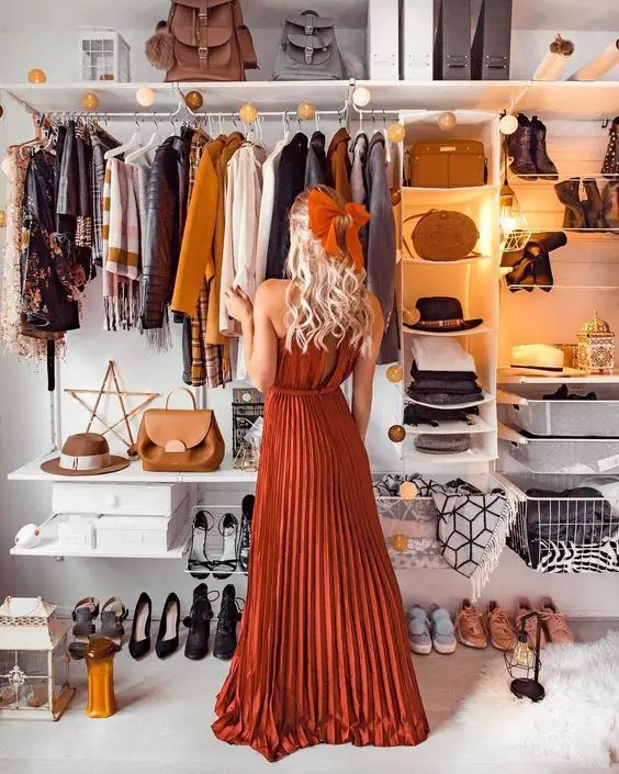 A woman standing in front of a wardrobe with clothes, bags and shirts in case she doesn't know what to wear