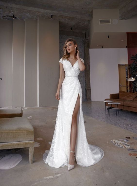 As a casual wedding dress, a woman wears a short-sleeved white maxi dress with a thigh-high slit.