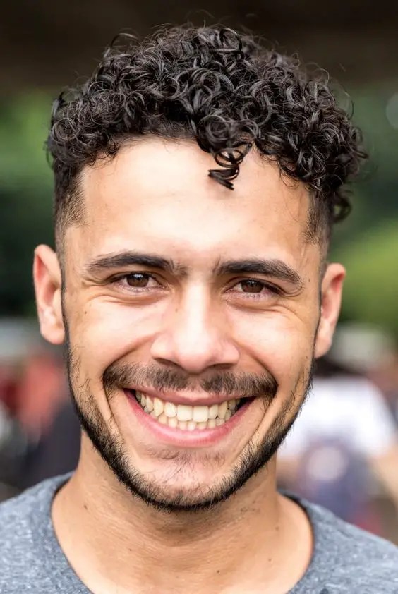 A man showing off his short curly hair with a smile