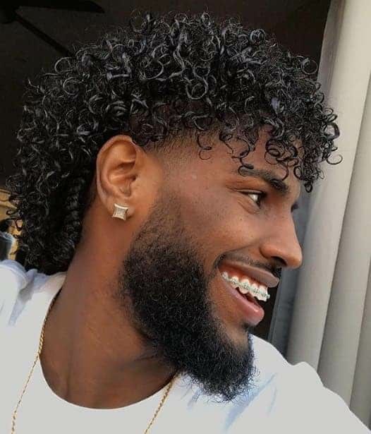 Man smiling and looking to the side while rocking shiny curly hairstyle for men
