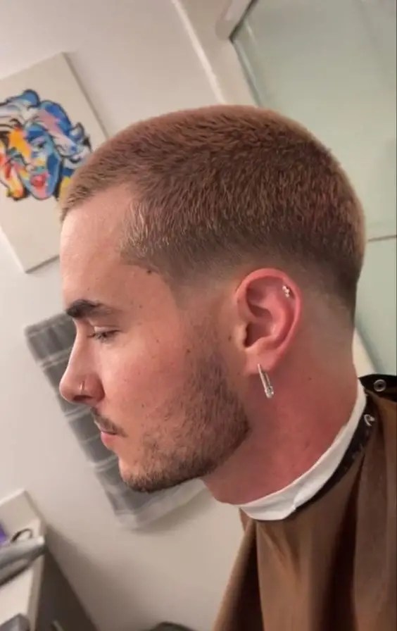 A man wearing earrings and showing a profile of his haircut