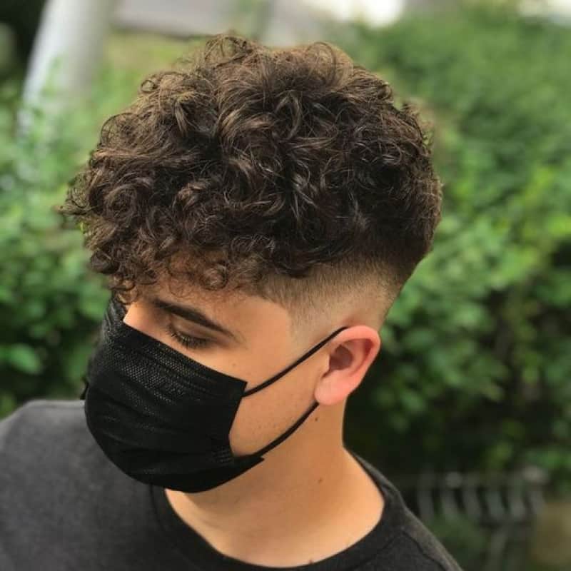 A man wearing a face mask is rocking his curly hair in a fade
