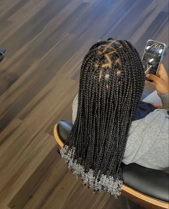 Woman showing off shoulder-length knotless braids with beads while holding mobile phone