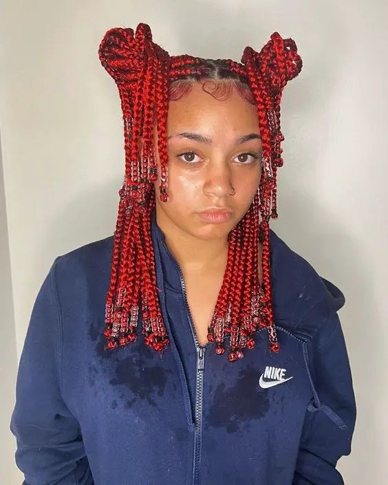 A woman with beaded red braids stuffed into a bun