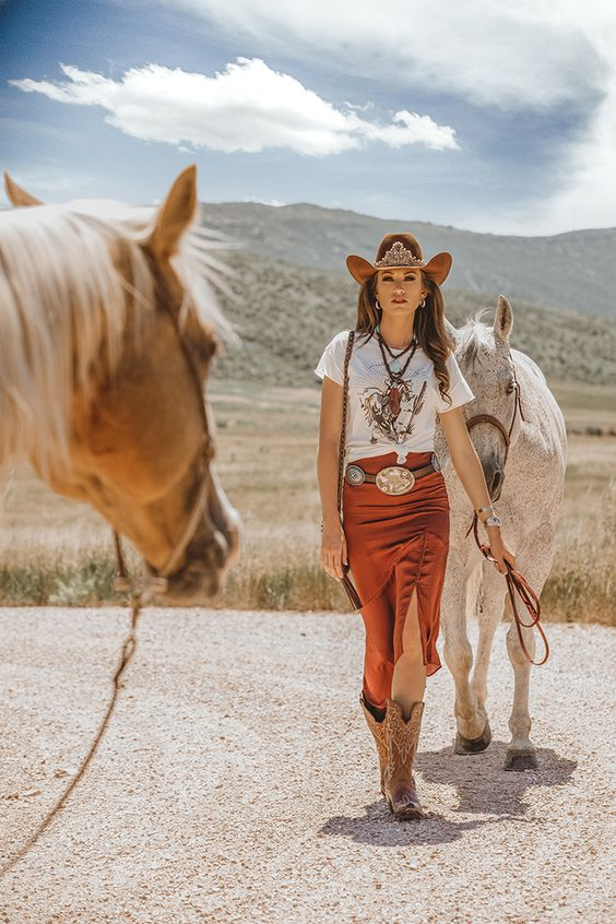 Woman wearing cowgirl outfit idea accompanied by midi skirt, t-shirt, belt, boots and cowgirl hat