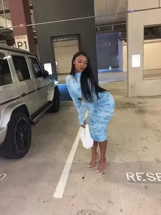 lady posing by a car in a dress with white bag
