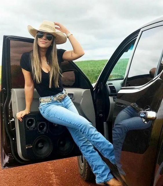 Woman in jeans, black top and cowgirl hat by car