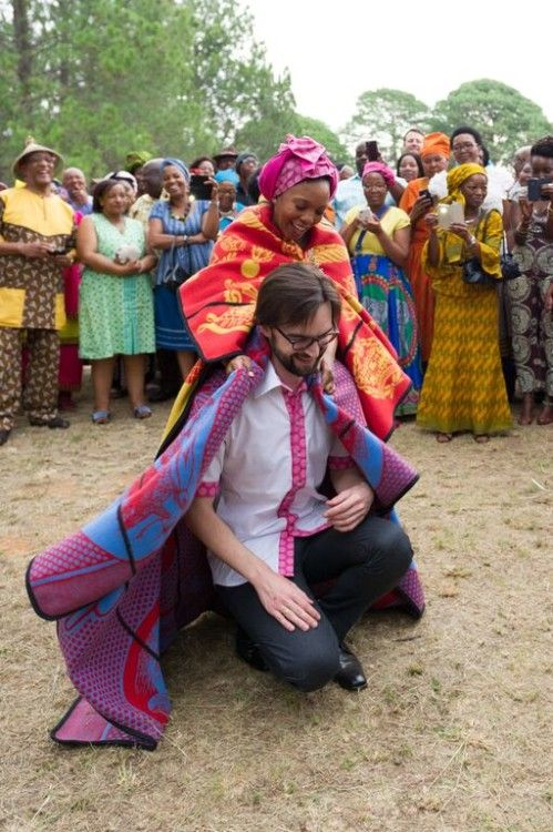 Smiling woman giving a traditional Sotho costume to a Caucasian man